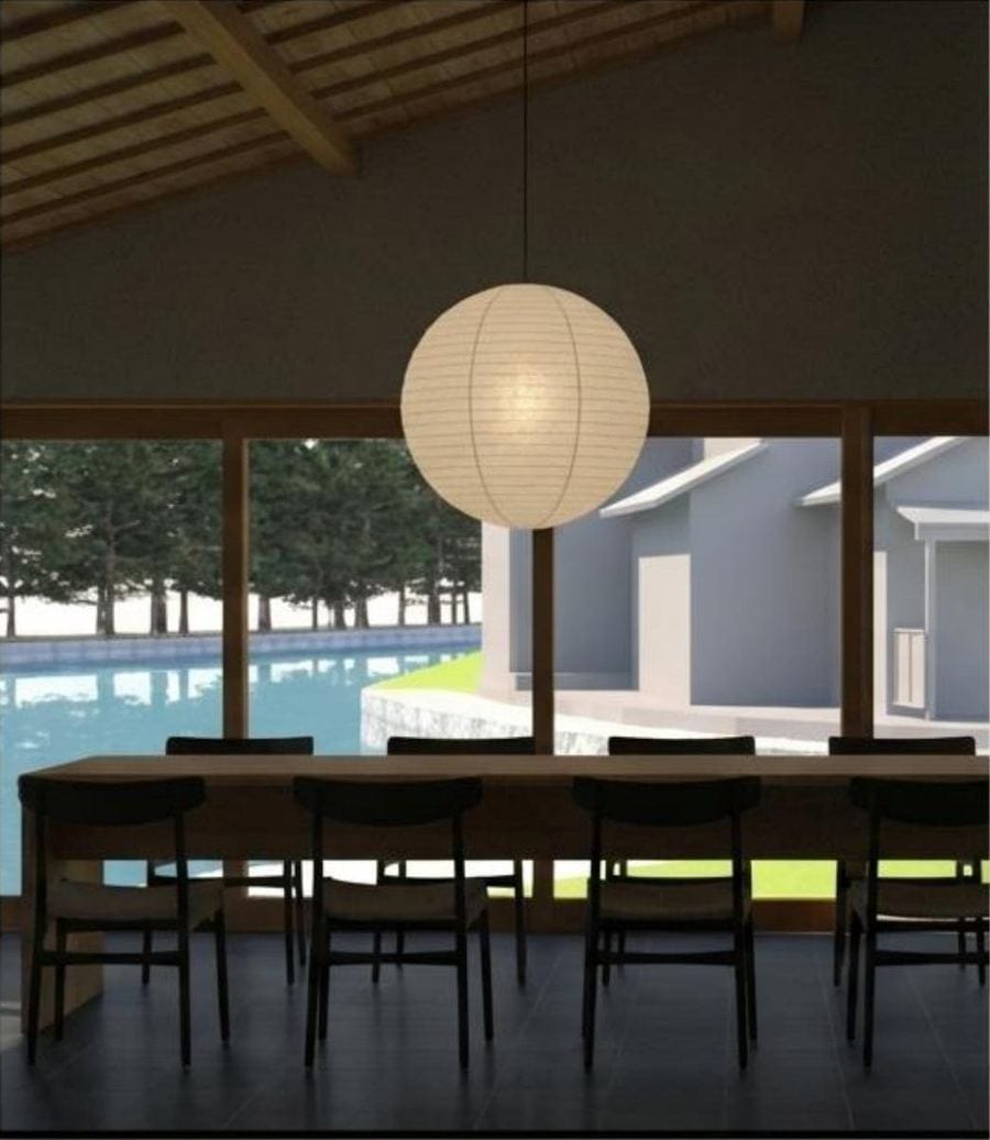 The dining room of the main house: a paper lantern hanging above a long timber table, with the Monju channel and pine trees through the windows beyond.